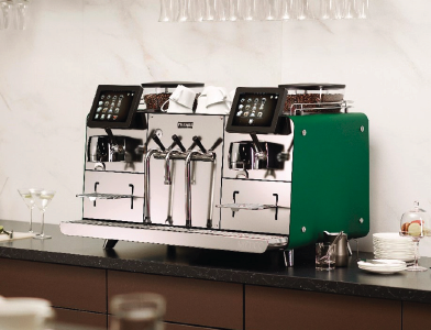 A Franke professional coffee machine with twin touch screens and green side panel on a bar counter